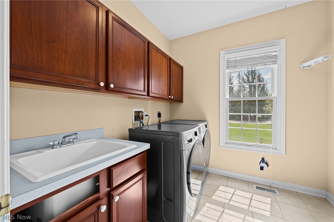 Laundry room with dark wood cabinetry, a utility sink, front-loading washer and dryer, and a lawn-facing window.