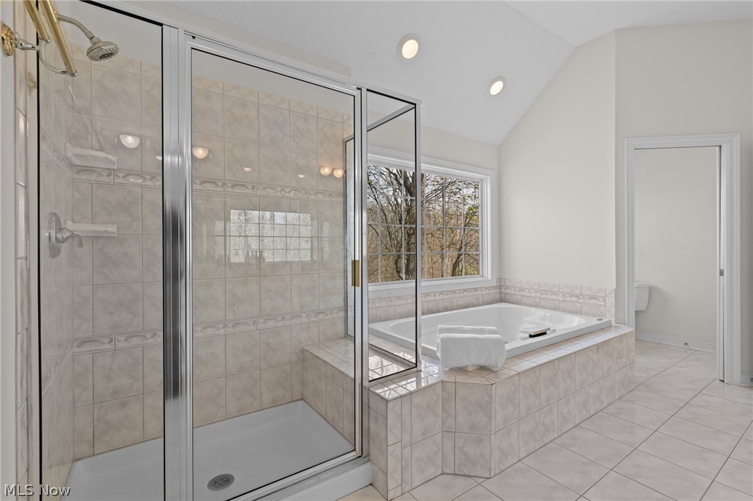 Tiled bathroom with a glass-enclosed shower and built-in jetted tub beside a large window.
