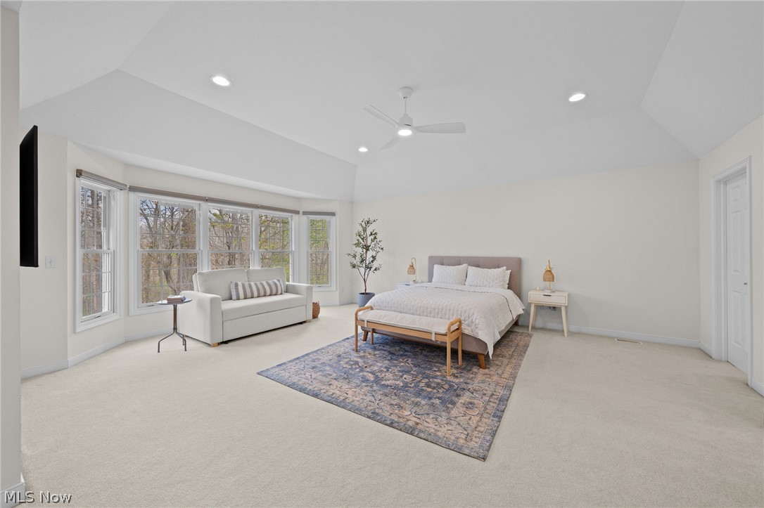 Staged bedroom with a white bed, vaulted ceiling, and large windows overlooking trees.