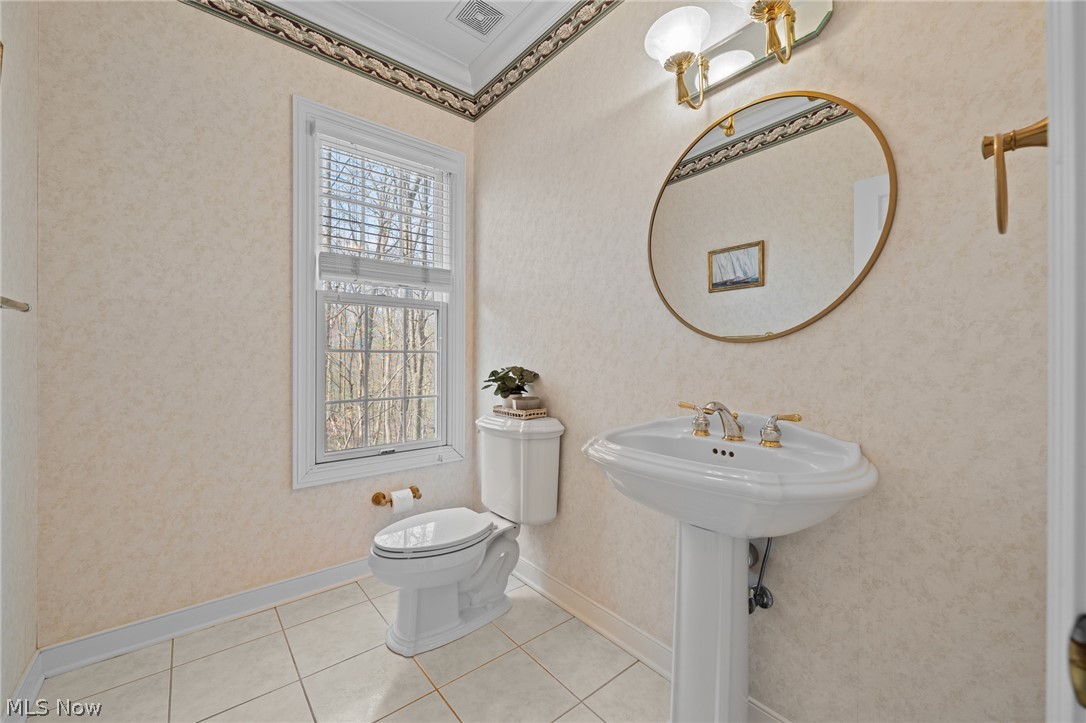 Powder room with a pedestal sink, oval mirror, toilet, and wooded view through the window.