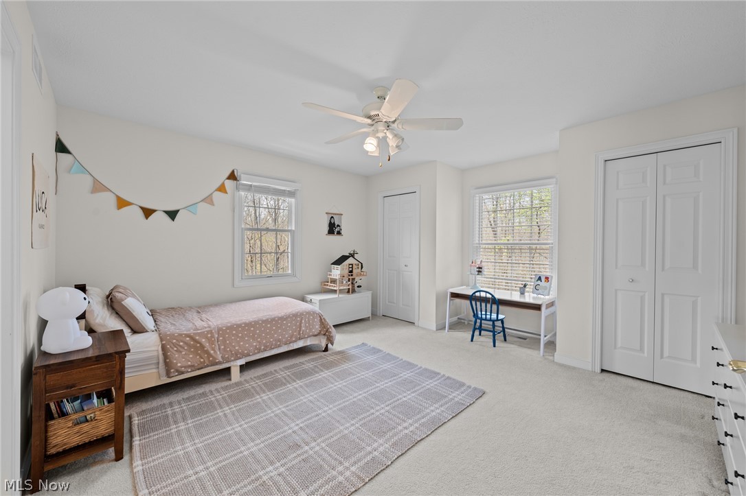 Bedroom with a single bed, toy house, and child-sized desk beneath two windows.