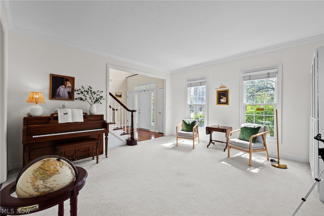Bright sitting room with an upright piano, a globe, and two chairs beside tall windows.