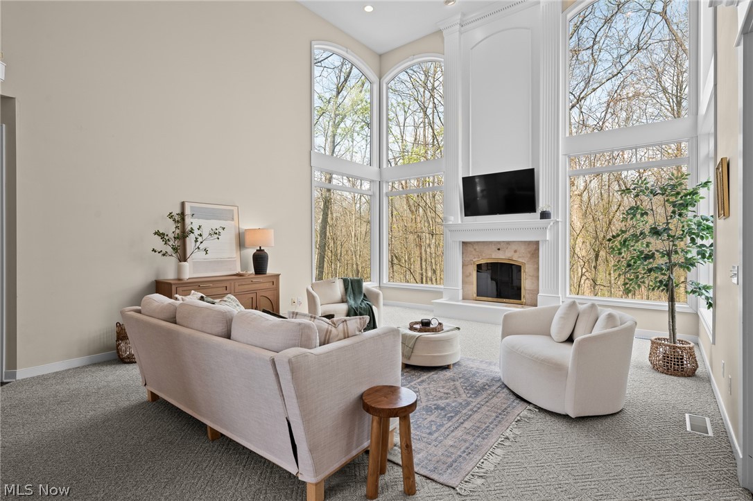 Living room with vaulted ceiling, tall windows overlooking trees, and a fireplace beneath a television.