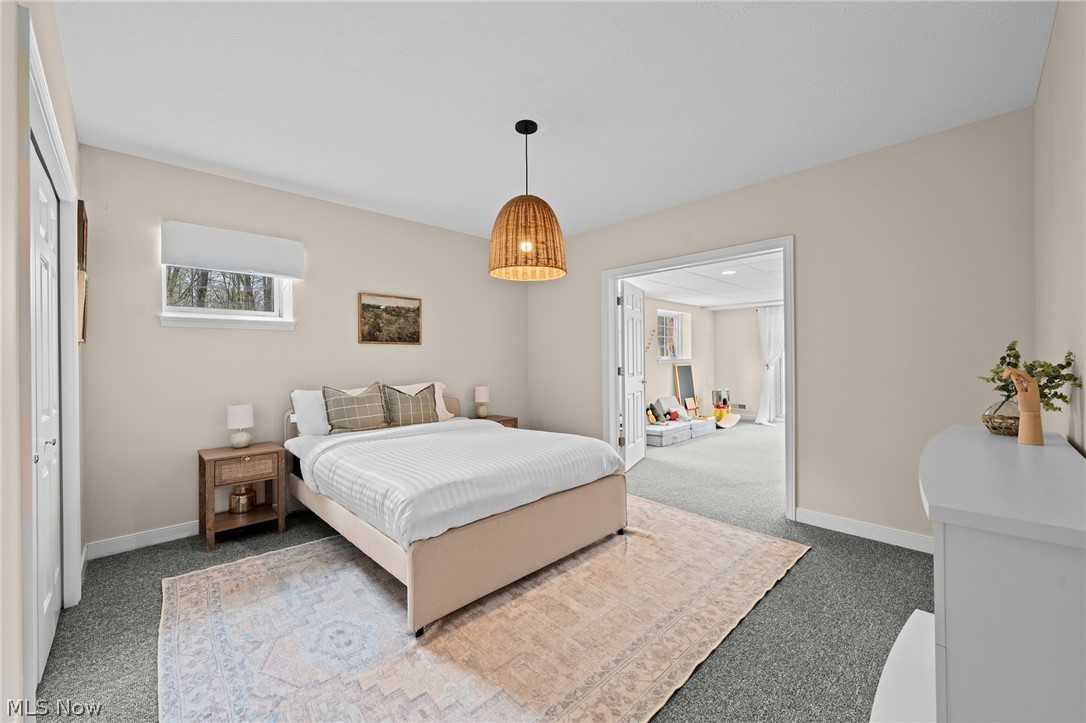 Staged bedroom with a queen bed, plaid pillows, and a doorway to an adjoining sitting room.