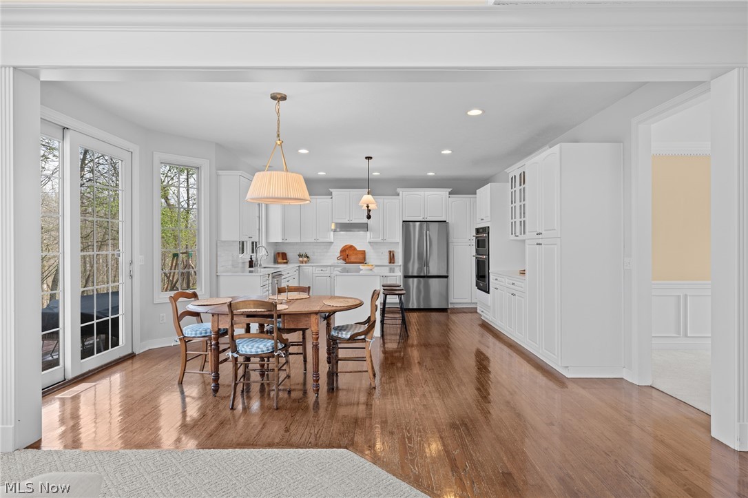 Kitchen and dining area with white cabinetry, stainless appliances, hardwood floors, and tall windows.