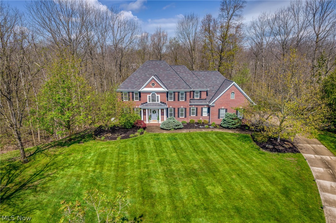 Aerial view of a red-brick home with a columned entrance, broad lawn, and mature trees.