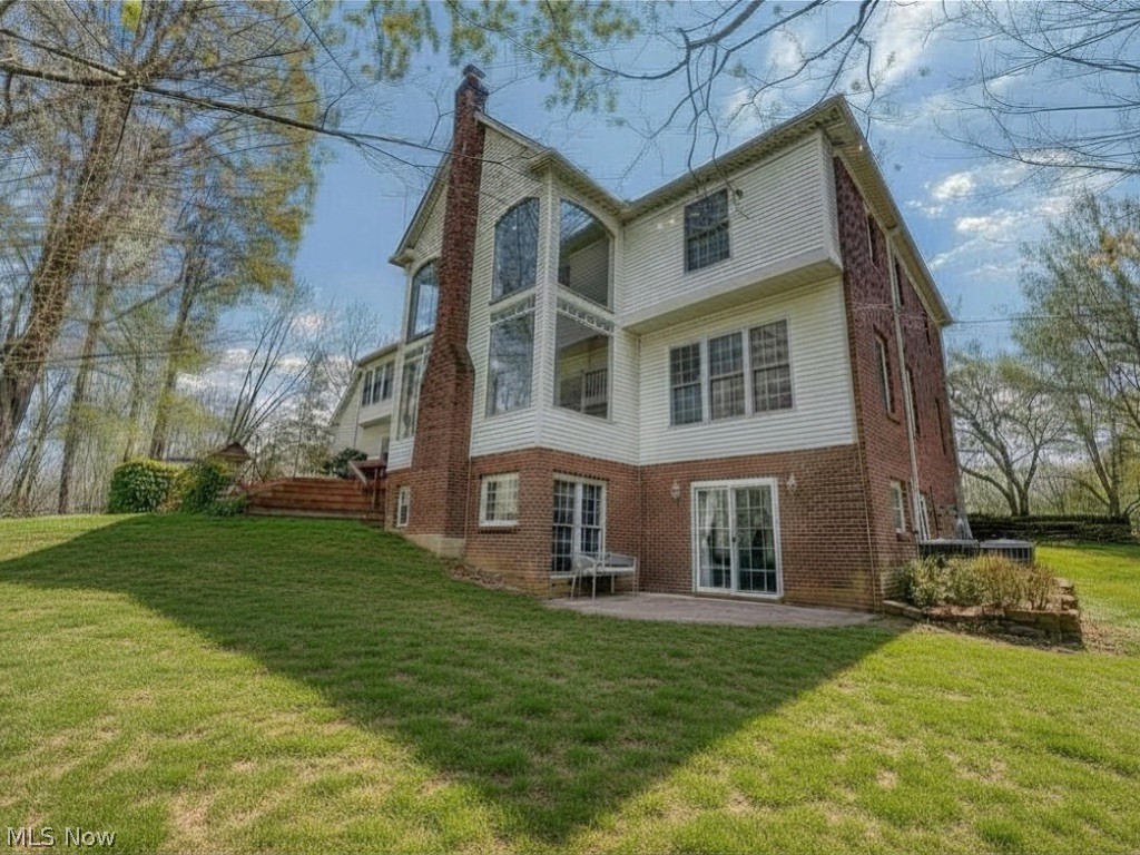 Rear of a two-story brick-and-siding home with a tall central window and walkout patio.