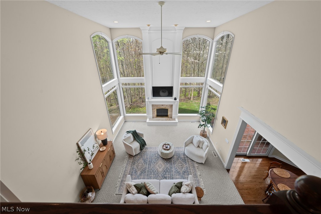 Two-story living room with tall windows overlooking trees and a fireplace beneath a television.