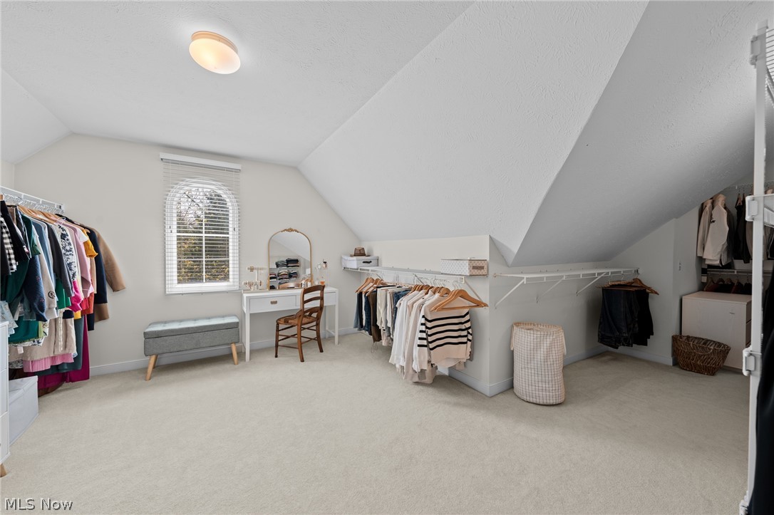 Walk-in closet with clothing racks, a vanity beneath an arched window, and a cushioned bench.