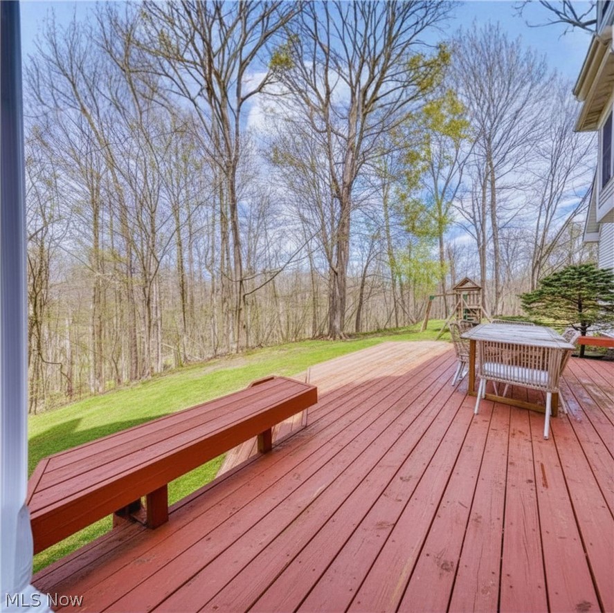 Wooden deck with bench and outdoor table overlooking a green lawn and wooded backyard.