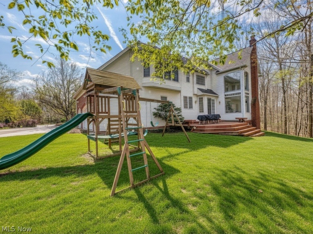 Rear exterior of a two-story home with a wooden deck and a play structure with green slide.