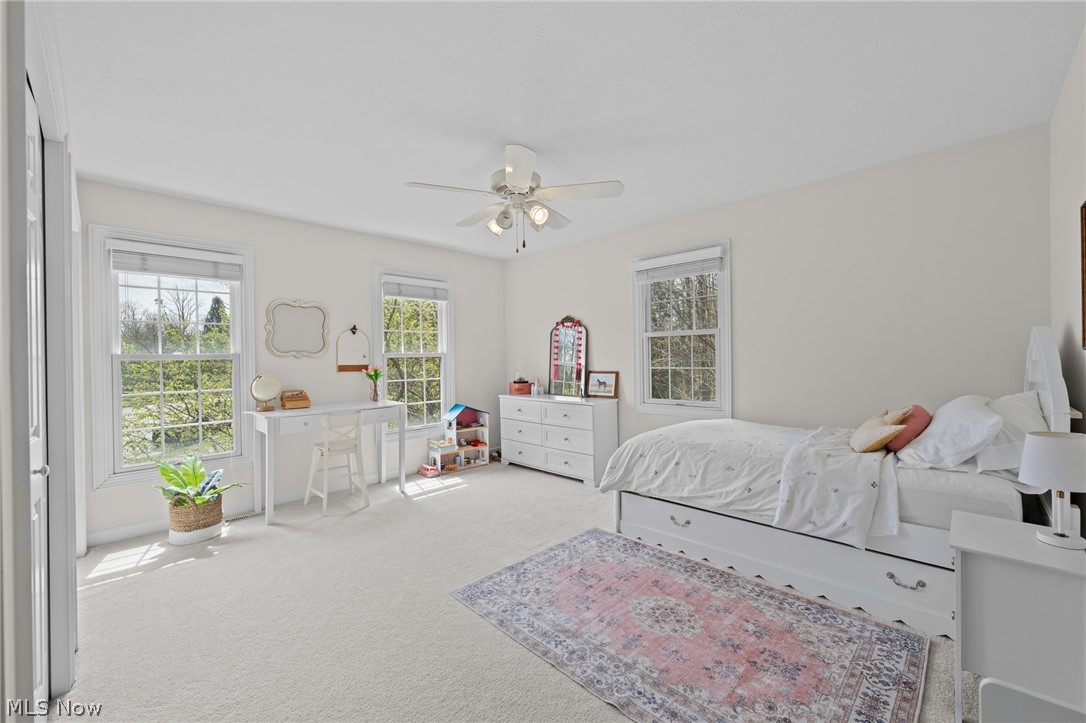 Bright bedroom with a white bed, three windows, a desk, and a patterned area rug.