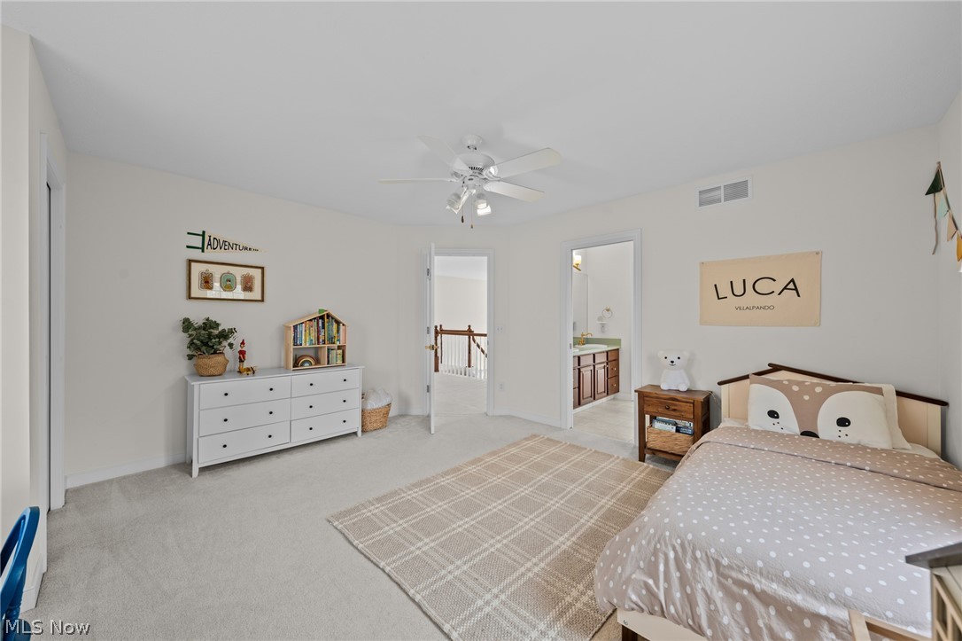 Furnished bedroom with taupe dotted bedding, a plaid rug, white dresser, and ceiling fan.