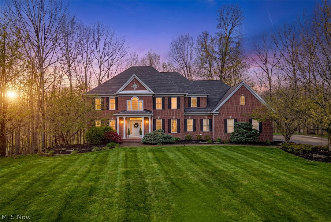 Two-story red-brick home with a broad lawn, photographed at dusk.