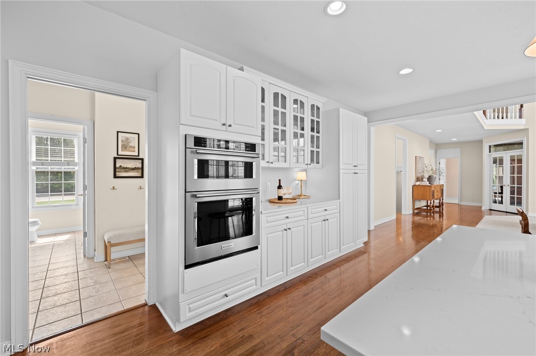 White kitchen with double wall ovens, glass-front cabinets, and a large island.