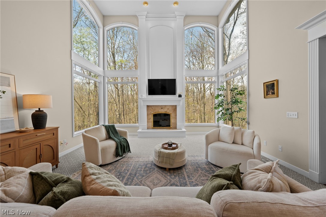 Staged living room with a white fireplace and expansive arched windows overlooking trees.