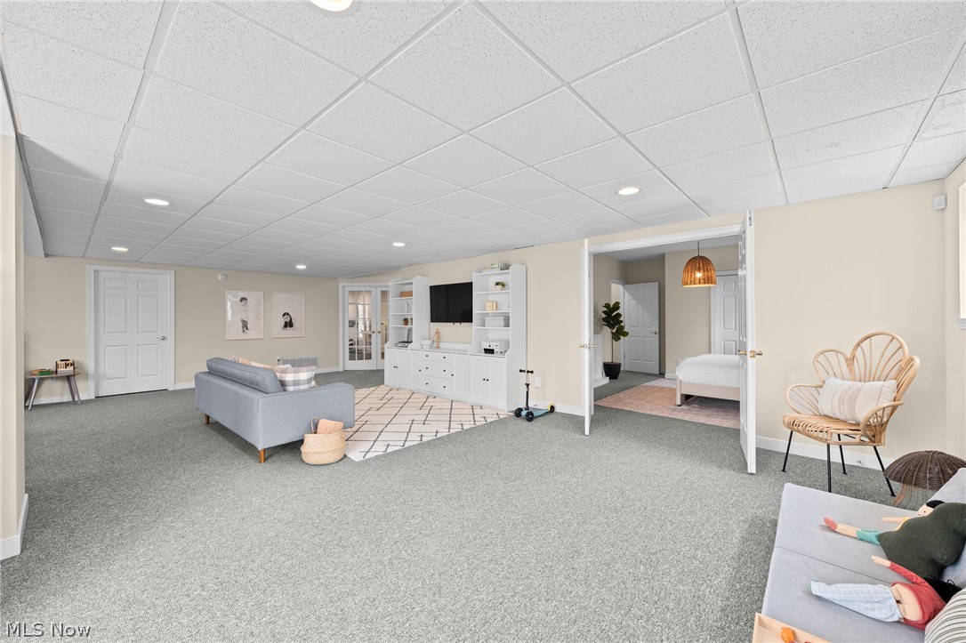 Finished lower-level family room with white built-ins, gray carpet, and open doors to a bedroom.