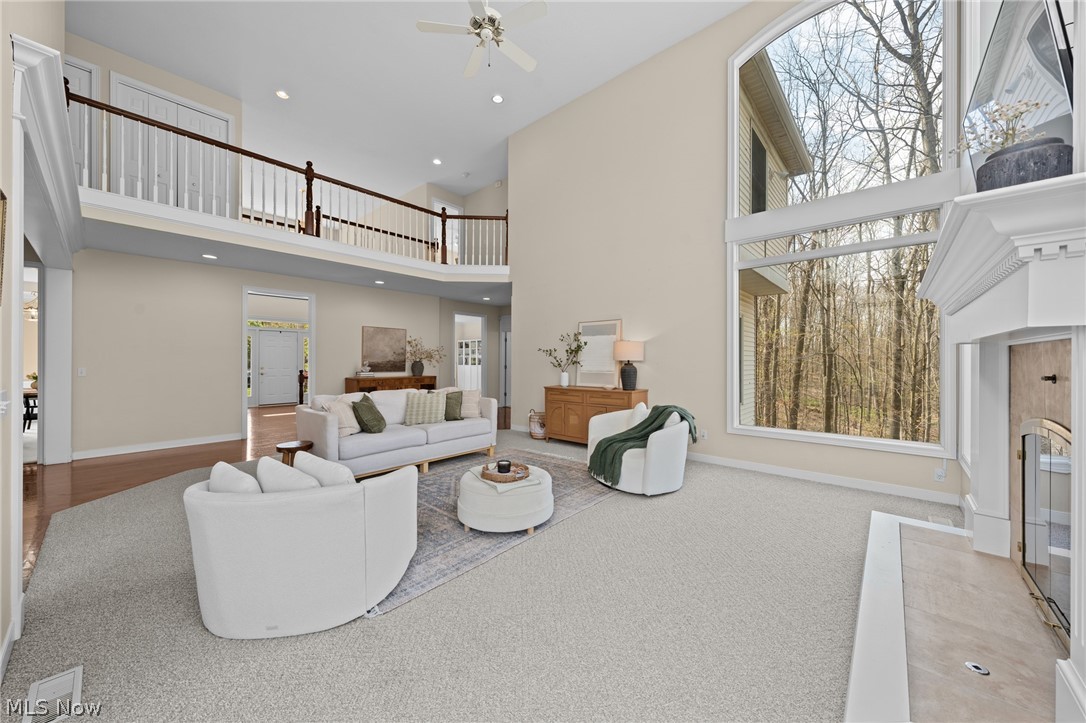 Two-story living room with white seating, a fireplace, and tall windows overlooking leafless trees.
