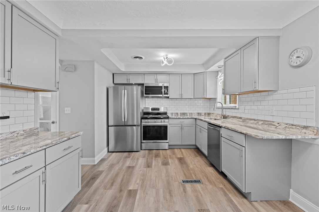 Kitchen with gray cabinetry, white subway tile, stainless steel appliances, and wood-look flooring.