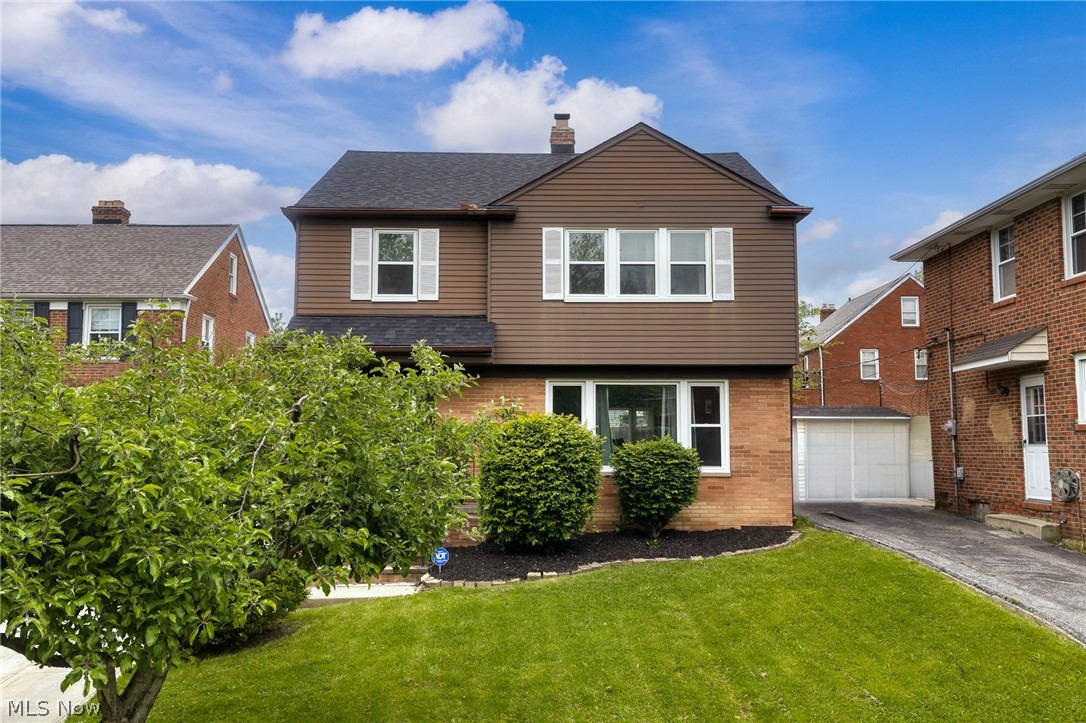 Two-story brown-and-brick house with white-trimmed windows, front lawn, shrubs, and driveway.