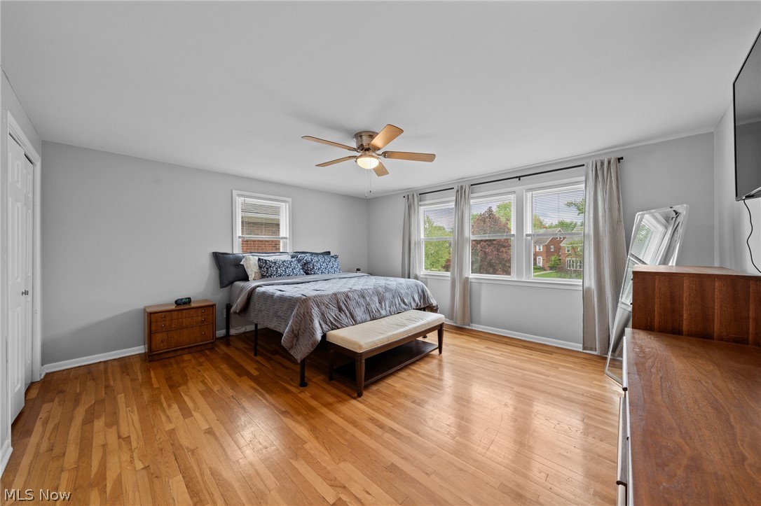 Bedroom with hardwood floors, a ceiling fan, and windows overlooking neighboring homes.