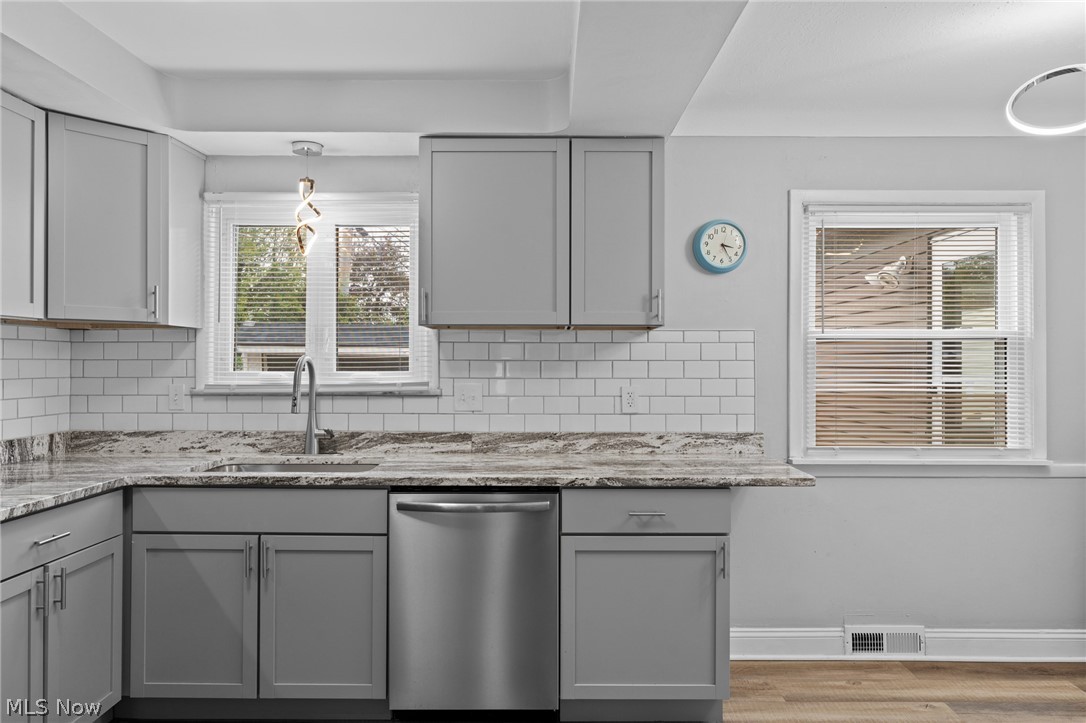 Kitchen with gray cabinets, granite counters, white subway tile, and a stainless steel dishwasher.