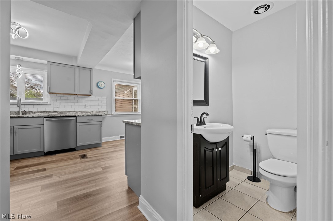 Kitchen and powder room with gray cabinetry, subway tile, wood-look flooring, and a dark vanity.