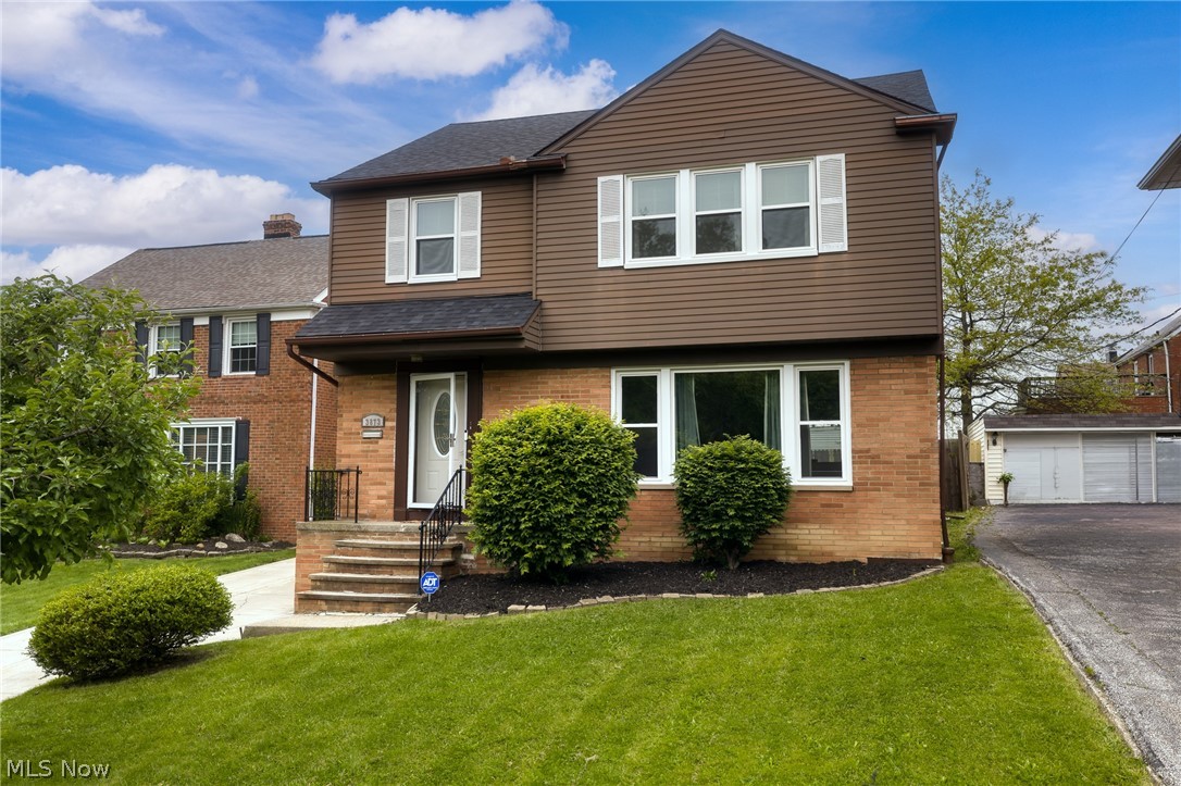 Two-story brick and brown-sided house with a small front porch and green lawn.