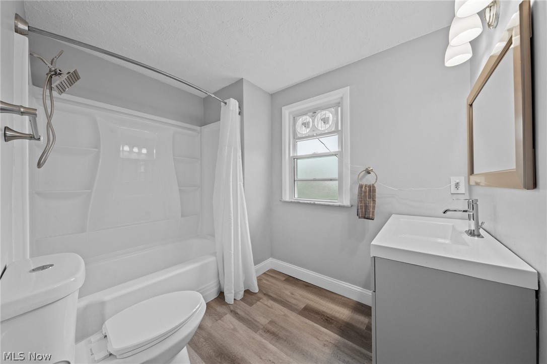 Bathroom with a white tub and shower, gray vanity, and wood-look flooring.