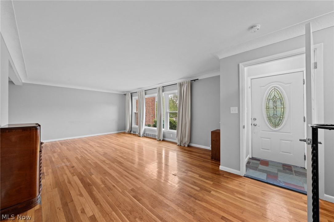Living room with hardwood floors, curtained windows, and a white stained-glass front door.