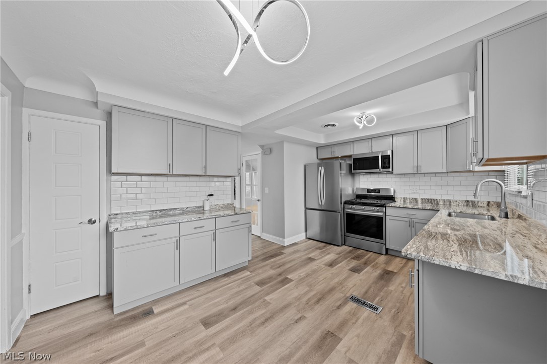 Kitchen with gray cabinets, granite counters, stainless steel appliances, and wood-look flooring.