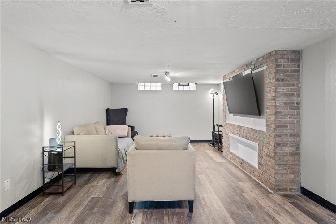Living room with light sofas, wood-look floors, and a brick fireplace wall with mounted TV.