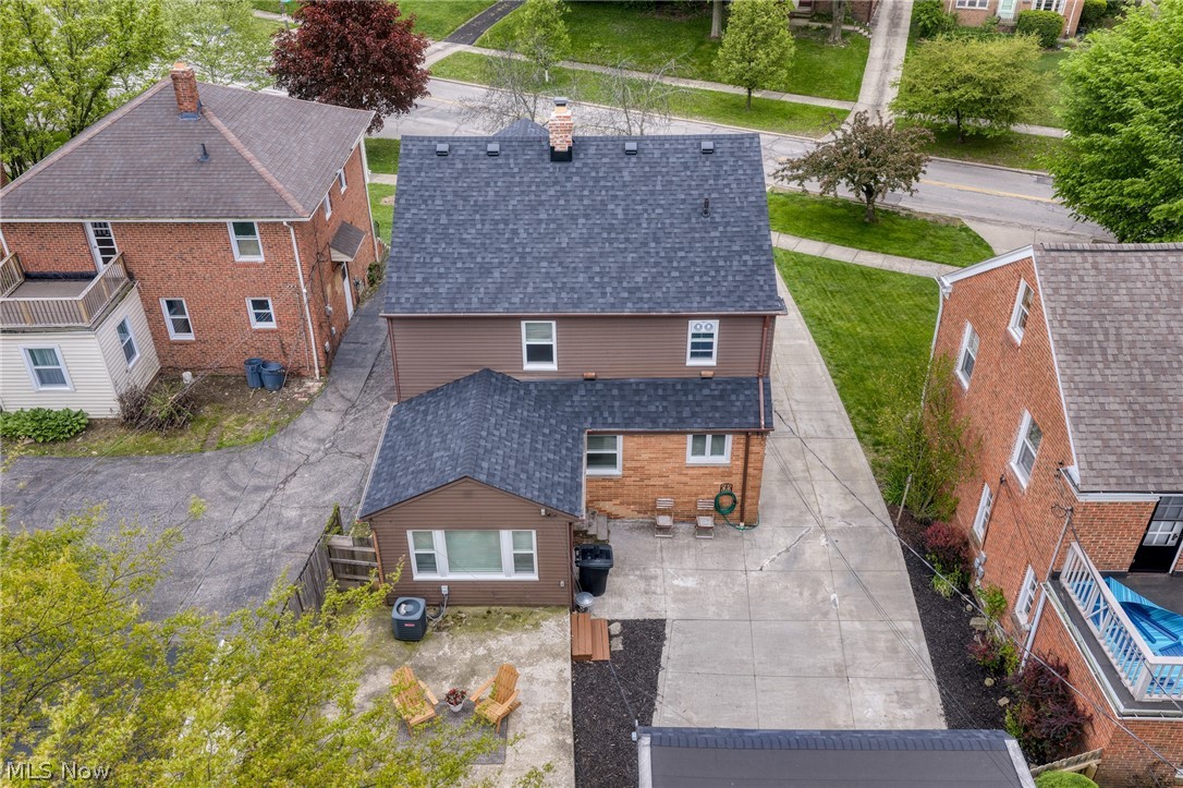 Aerial view of the home's rear, driveway, patio, and neighboring houses.