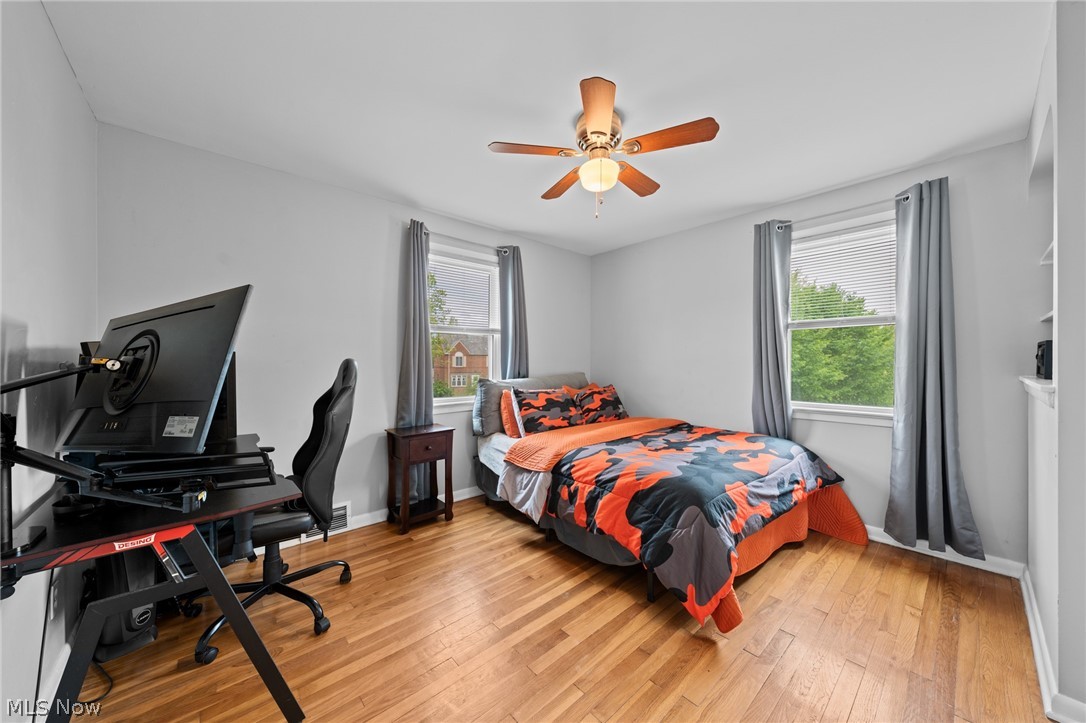 Bedroom with orange camouflage bedding, hardwood floors, and a computer gaming setup.