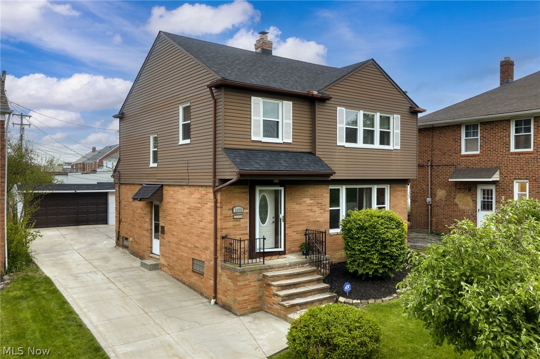 Two-story brick and brown-sided home with a concrete driveway leading to a detached garage.
