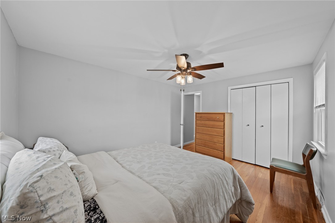 Bedroom with a large bed, hardwood floors, ceiling fan, and white closet doors.
