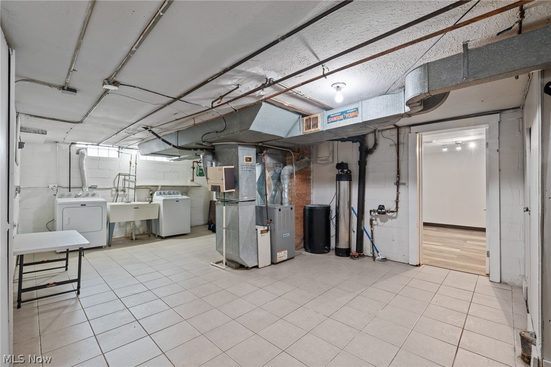 Basement laundry and utility room with washer, dryer, exposed ductwork, and tiled floor.