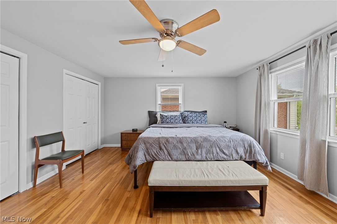 Bedroom with a king-size bed, hardwood floors, ceiling fan, and large curtained windows.