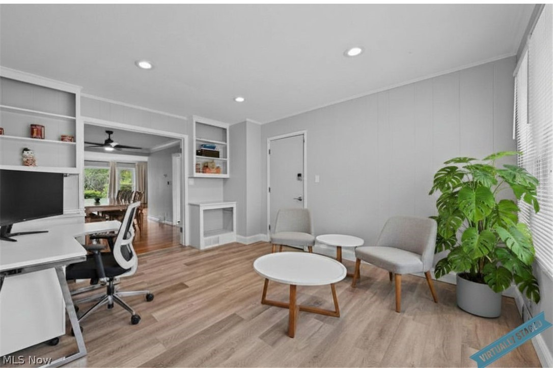 Sitting room with gray lounge chairs, round tables, and a large leafy plant beside a desk.