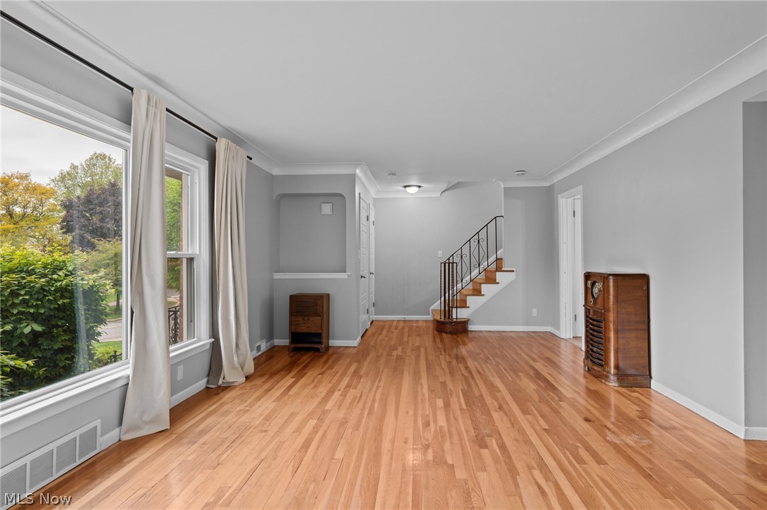 Living room with polished hardwood floors, tall curtained windows, and a staircase with a decorative railing.