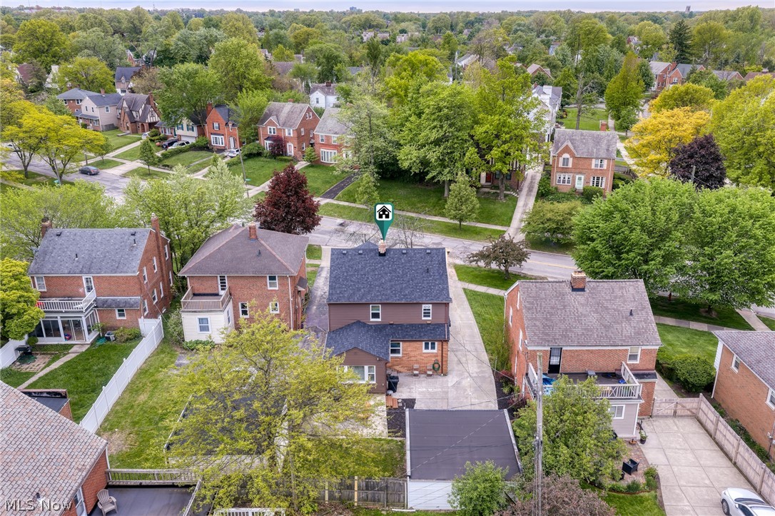Aerial view of a brick home with a driveway and detached garage on a tree-lined residential street.