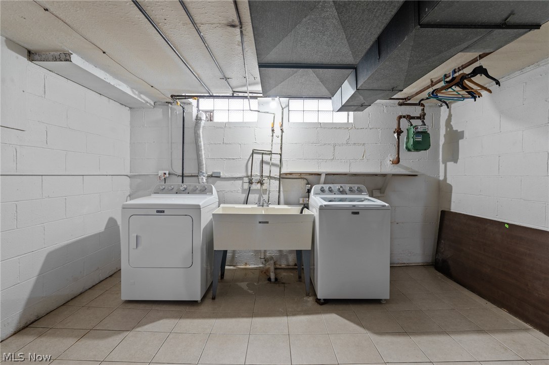 Basement laundry room with washer, dryer, and utility sink beneath exposed ceiling ductwork.