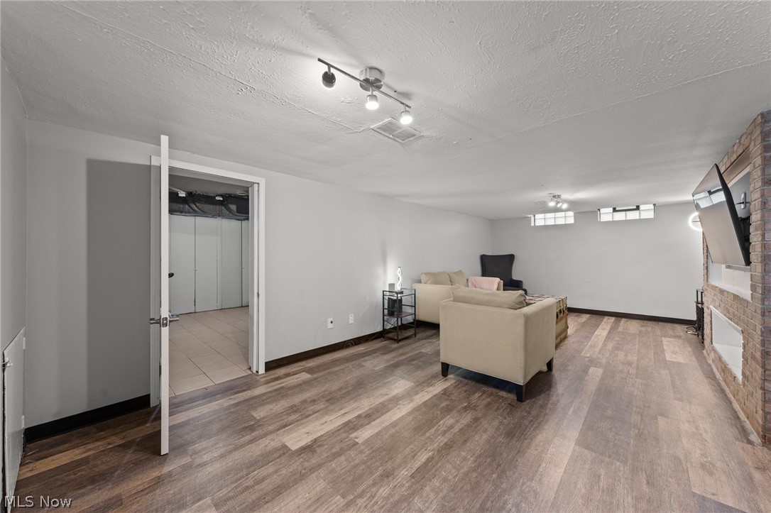 Furnished basement living area with beige sofas, plank flooring, and a brick wall with a mounted television.