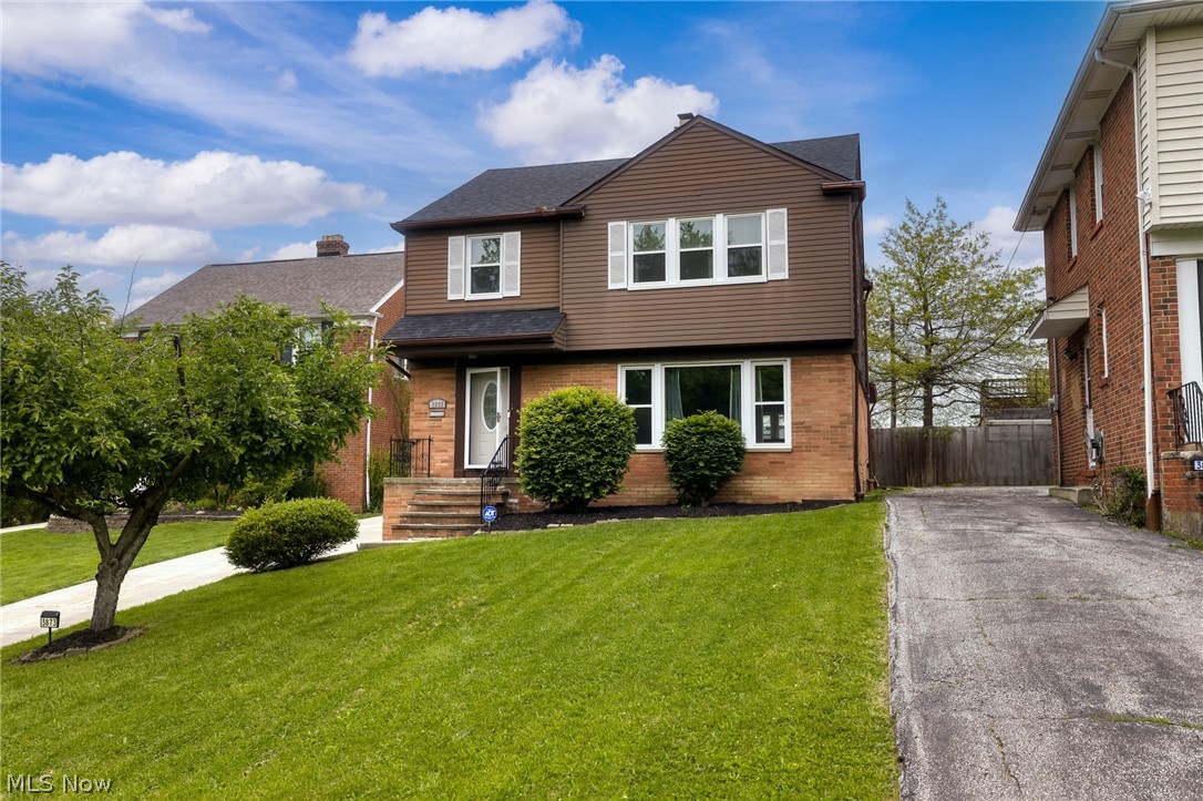 Two-story brick-and-siding home with a green front lawn, trimmed shrubs, and a driveway.