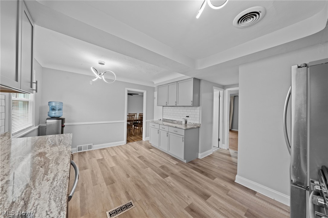 Updated kitchen with white cabinets, granite counters, wood-look floors, and a stainless steel refrigerator.