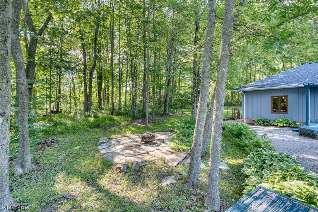Wooded backyard patio with a fire pit beside a blue-sided house.