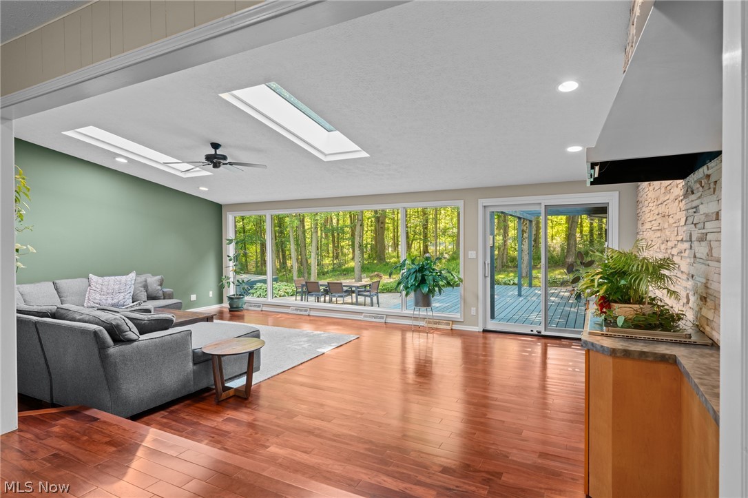 Living room with a gray sectional, stone fireplace wall, and large windows facing the woods.