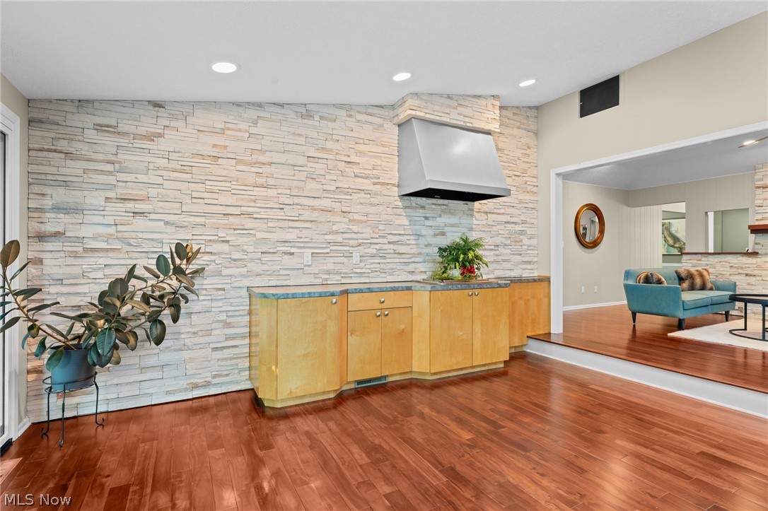 Kitchen with a full-height stone backsplash, wood cabinetry, and a stainless steel range hood.