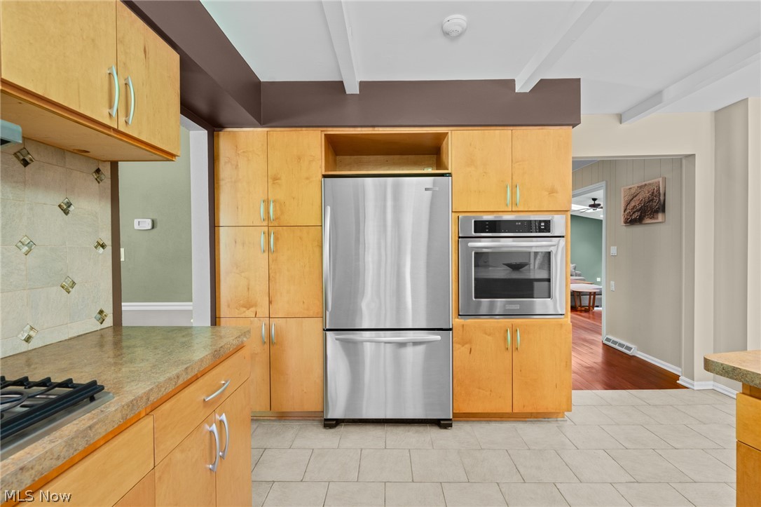 Kitchen with honey-colored cabinets, stainless steel appliances, and a stone countertop with a gas cooktop.