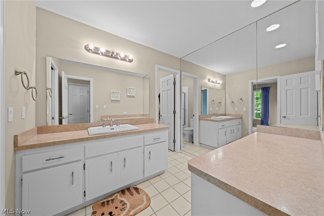 Spacious bathroom with white vanities, tan countertops, tiled floors, and a large wall mirror.